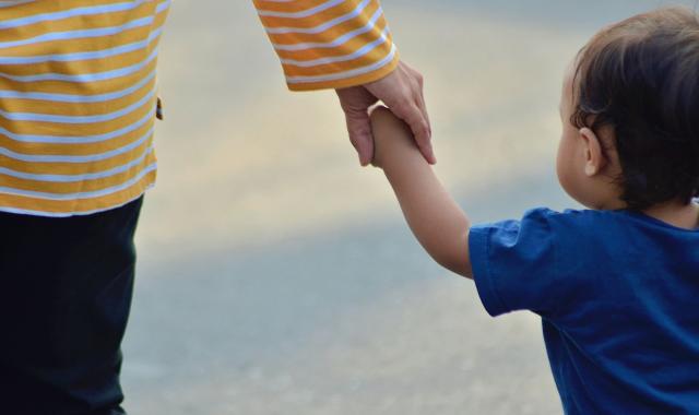 A photo of a person and a baby walking hand in hand.